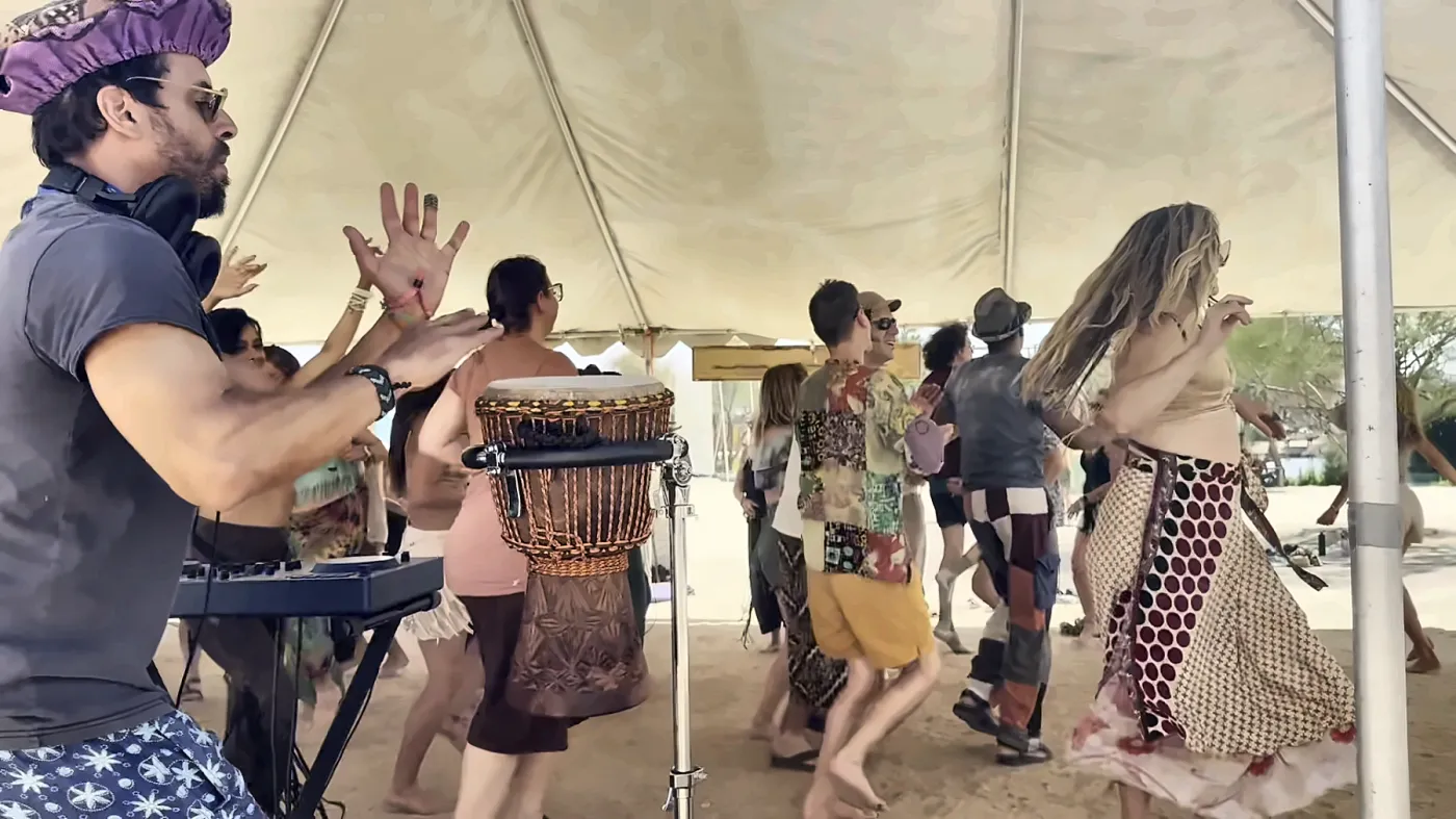 Taïb with his hands up behind the djembe at a daytime desert party