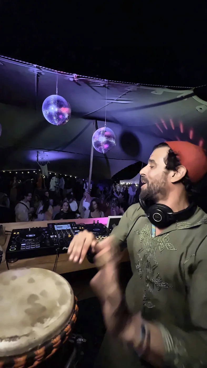 Taïb in a red fez drumming at Migrino, the crowd and disco balls behind him