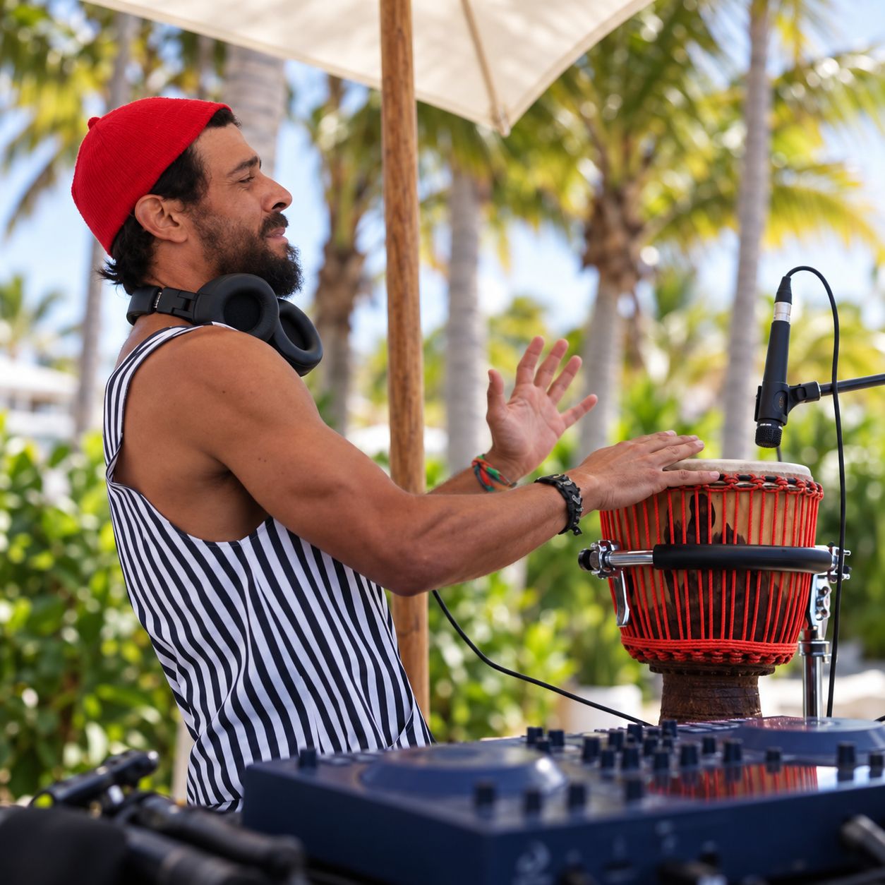 Taïb playing djembe beside his controller under palm trees